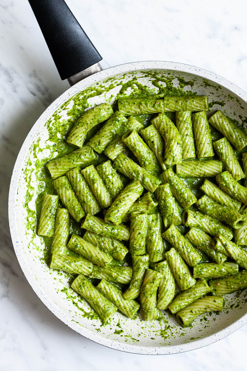 White frying pan with tortiglioni pasta covered in green paste