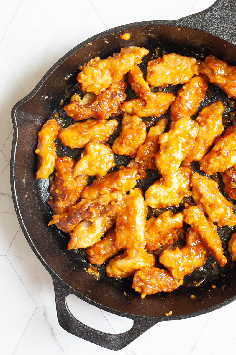 A black cast-iron skillet from above with sticky brown battered strips.