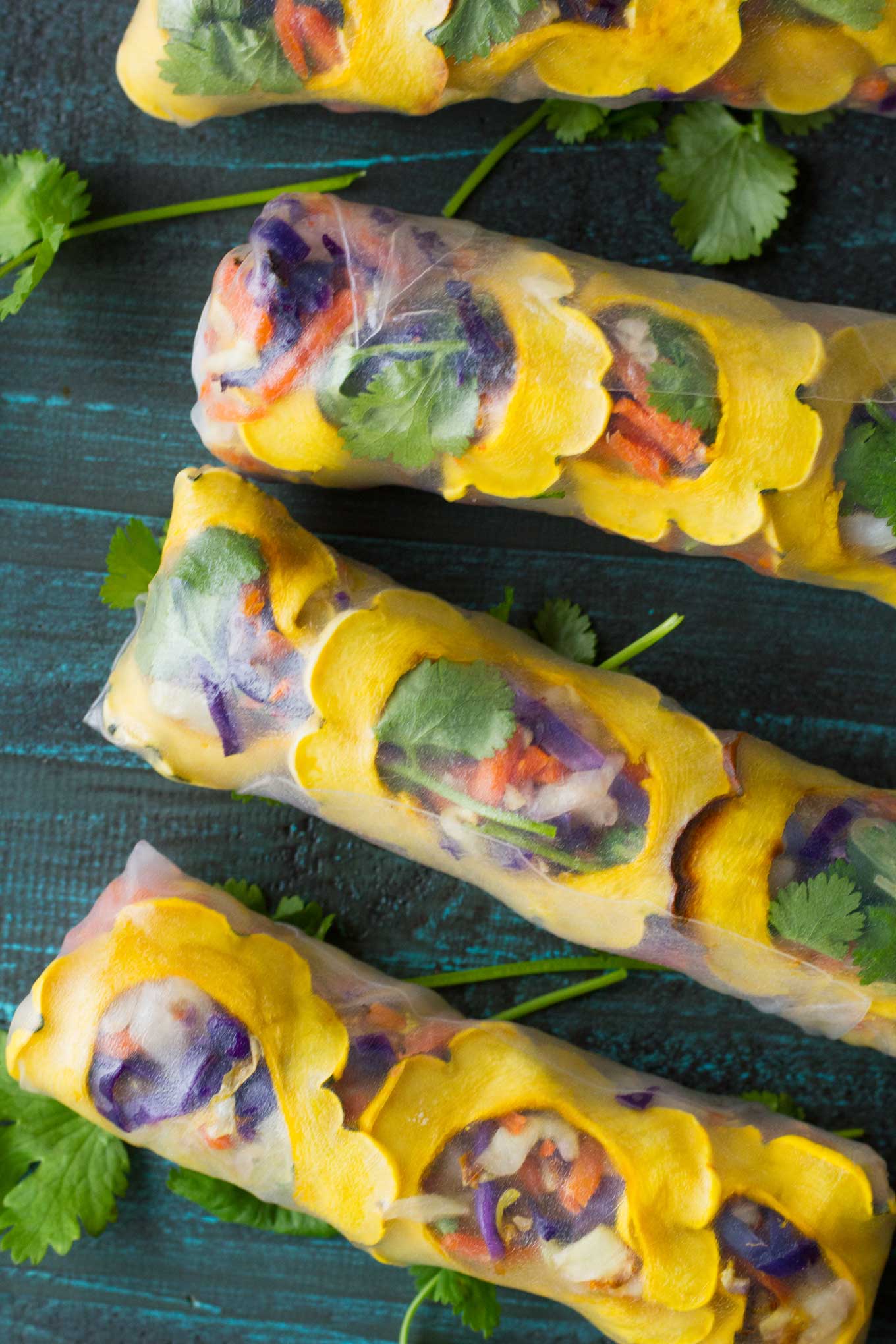 Rice paper rolls filled with yellow delicata squash slices, and other red purple and green ingredients.