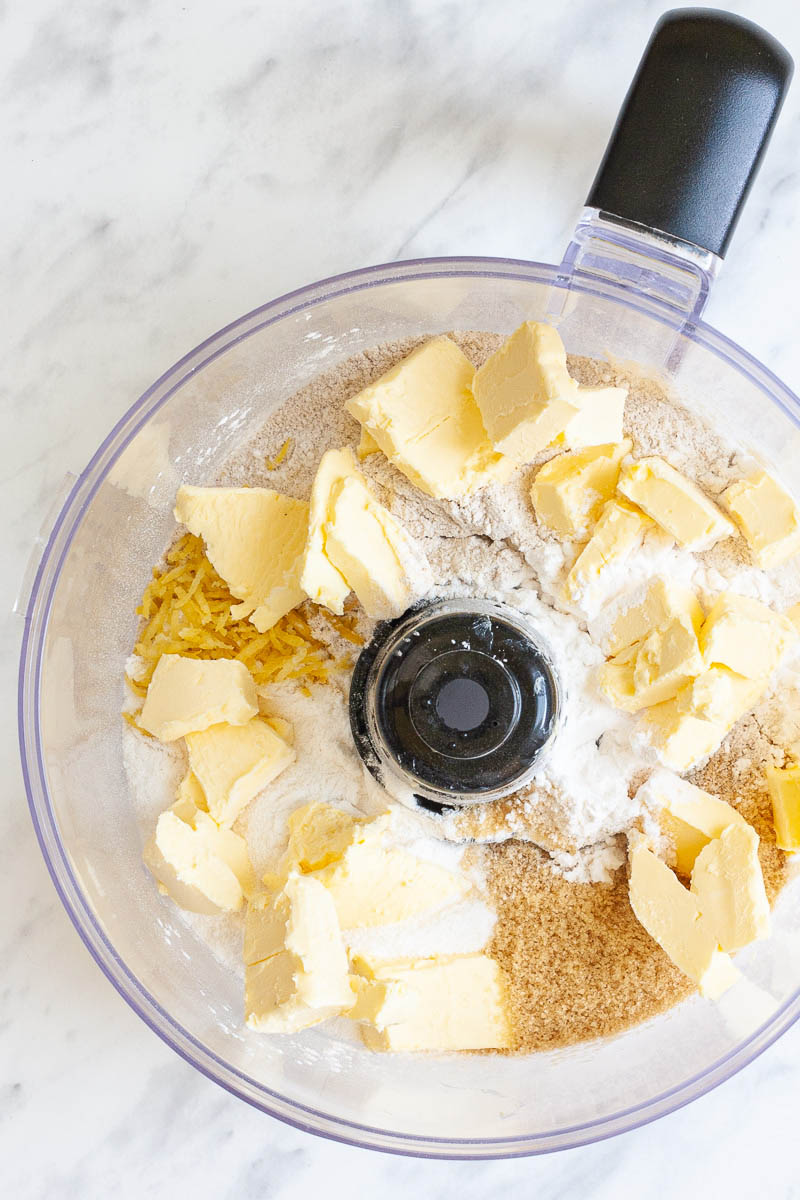 A food processor from above with cubed butter, flour, sugar and lemon zest. 
