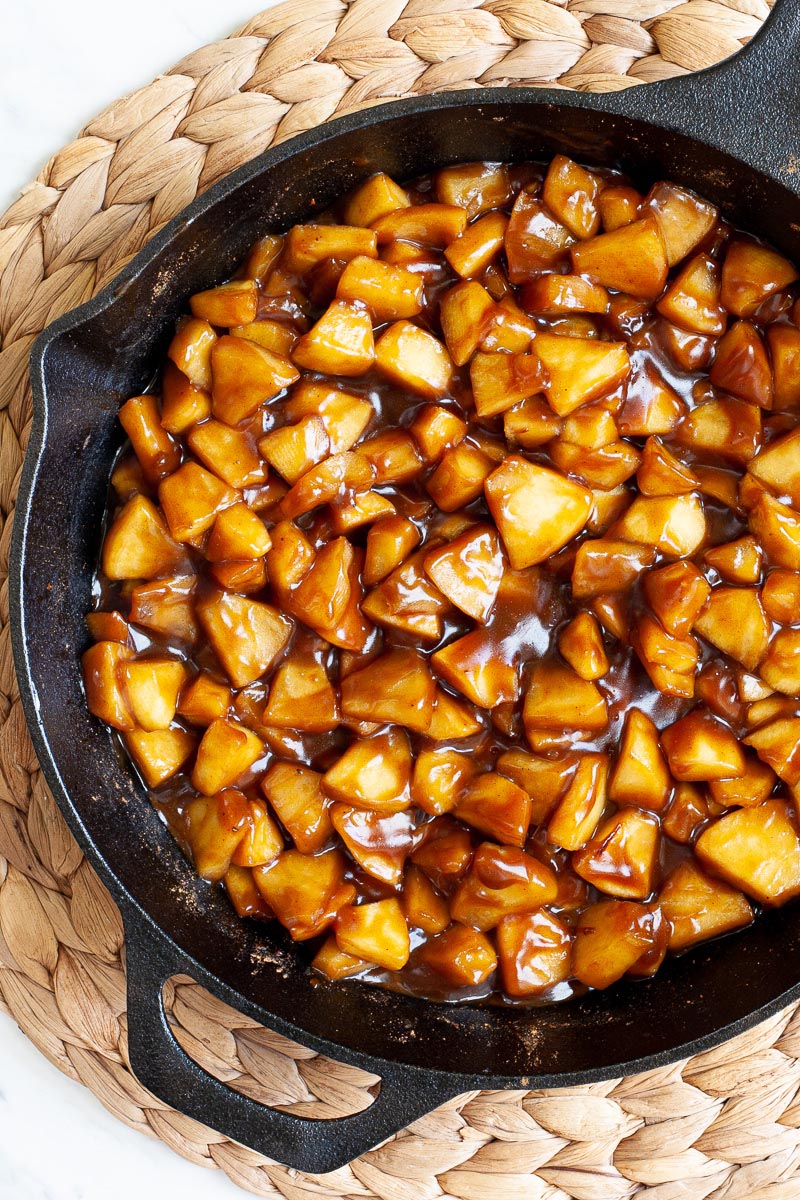 A black skillet from above with diced apples in caramel sauce.