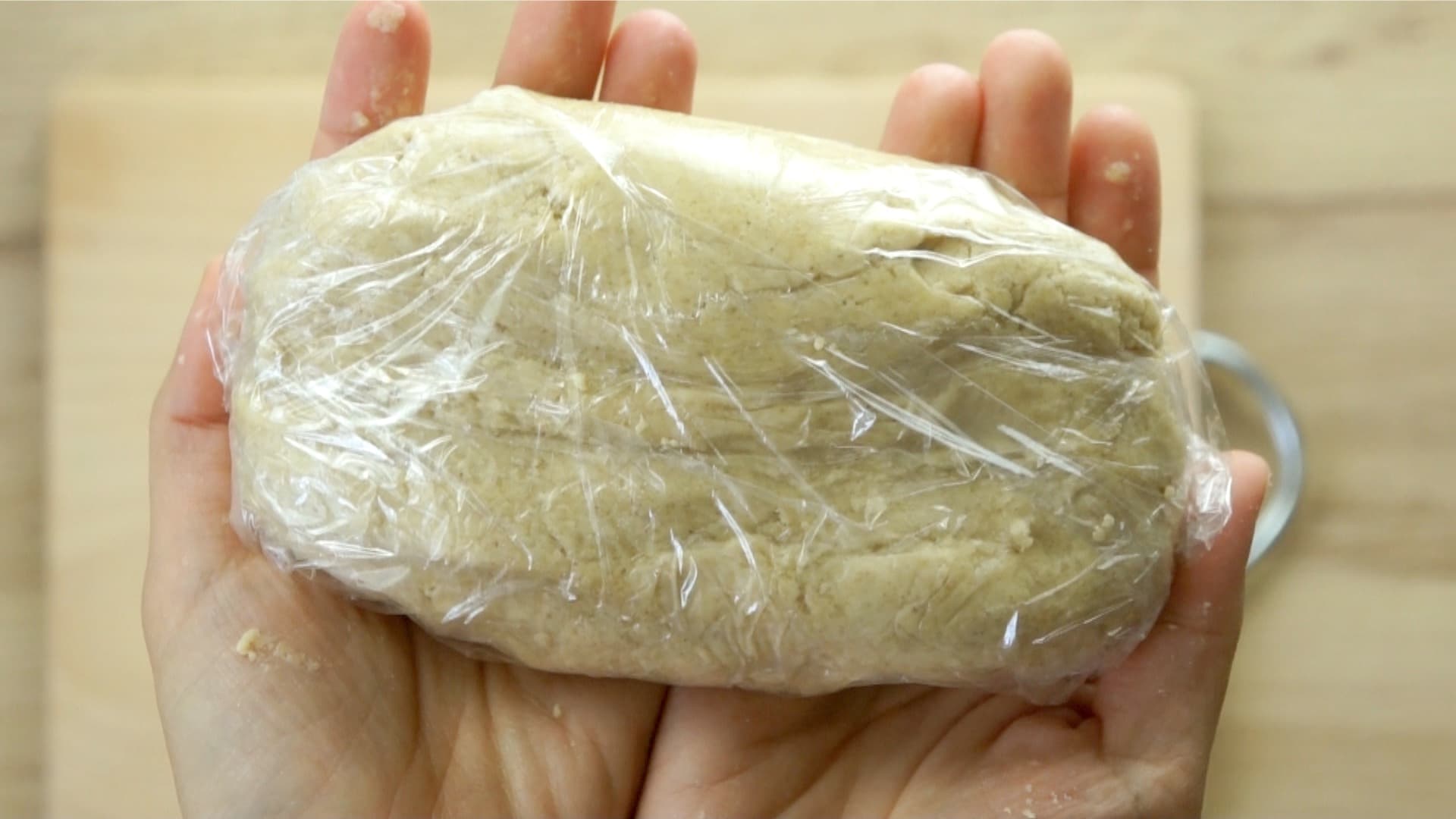 Hands are holding a dough shaped like a brick wrapped in plastic wrap.