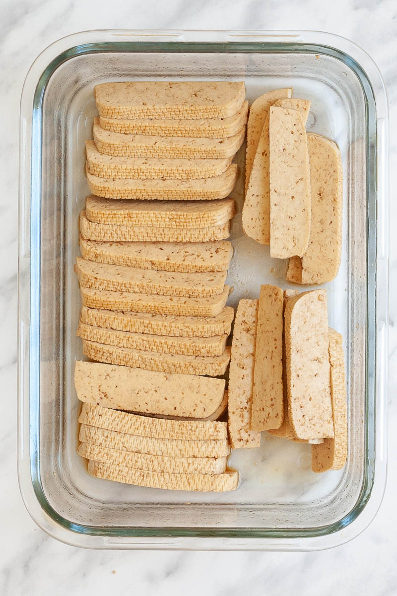 A glass bowl with think 1-inch wide and 3-inch long light brown tofu slices. 