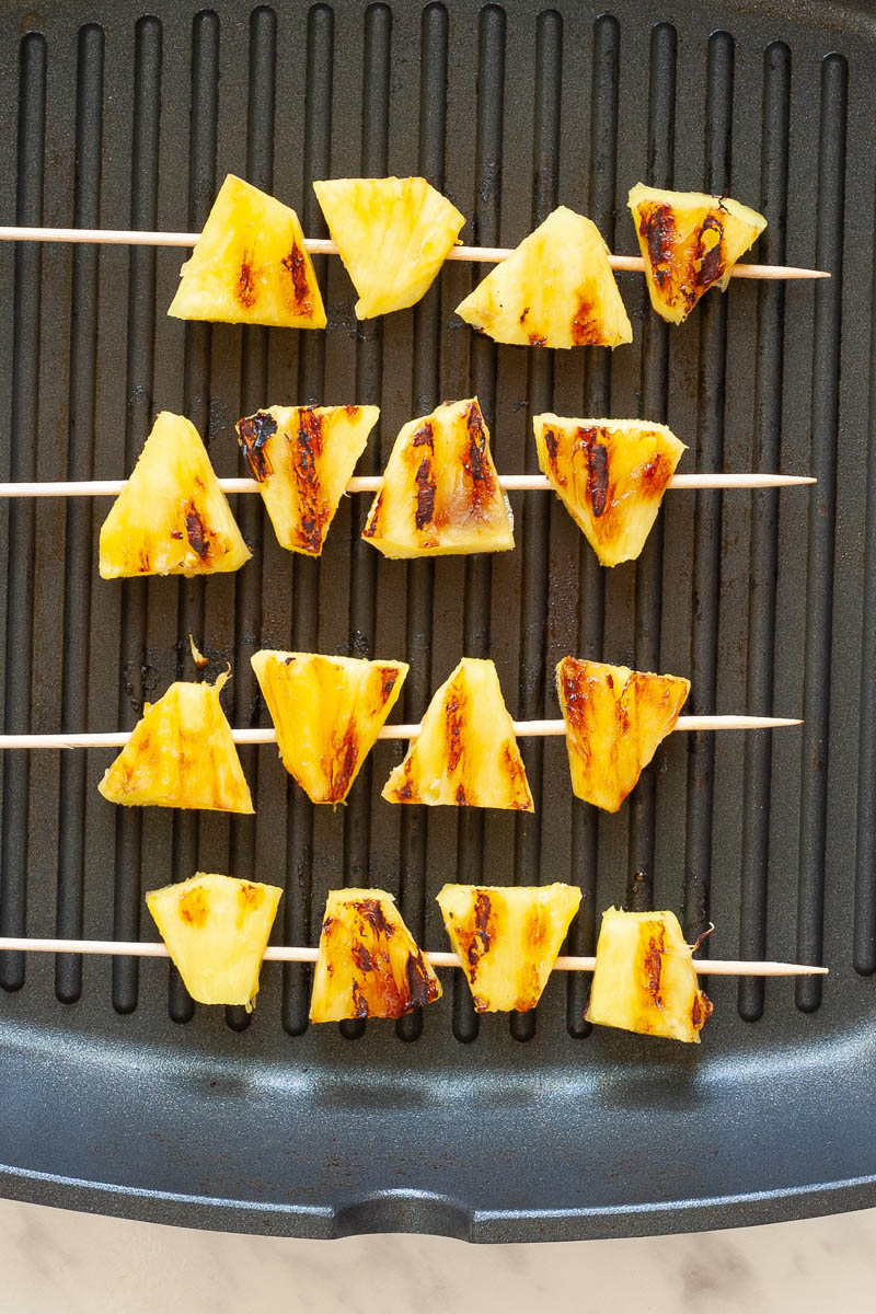 Charred pineapple wedges pierced with a skewer on a black grill pan