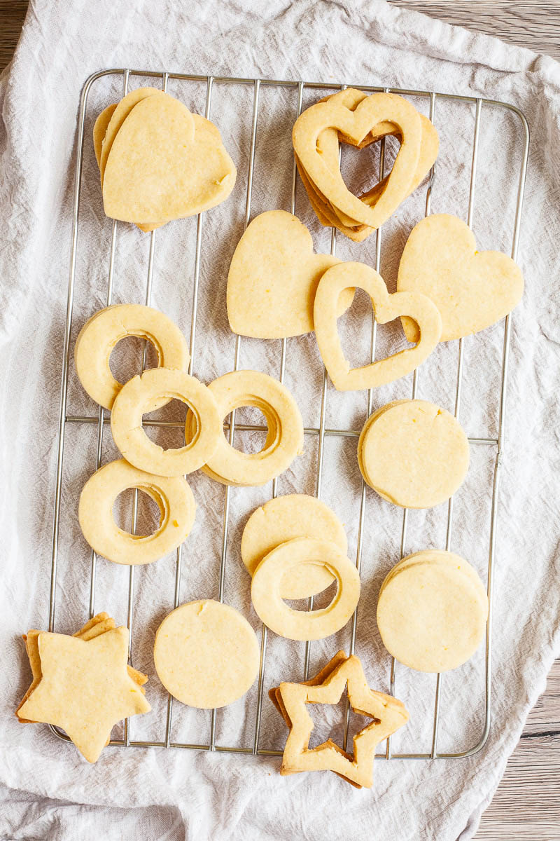 Light brown cookies in shapes of heart, star and circle are scattered on a wire rack.