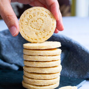 A stack of thin round cookies on a black board. A hand is holding the top cookie.