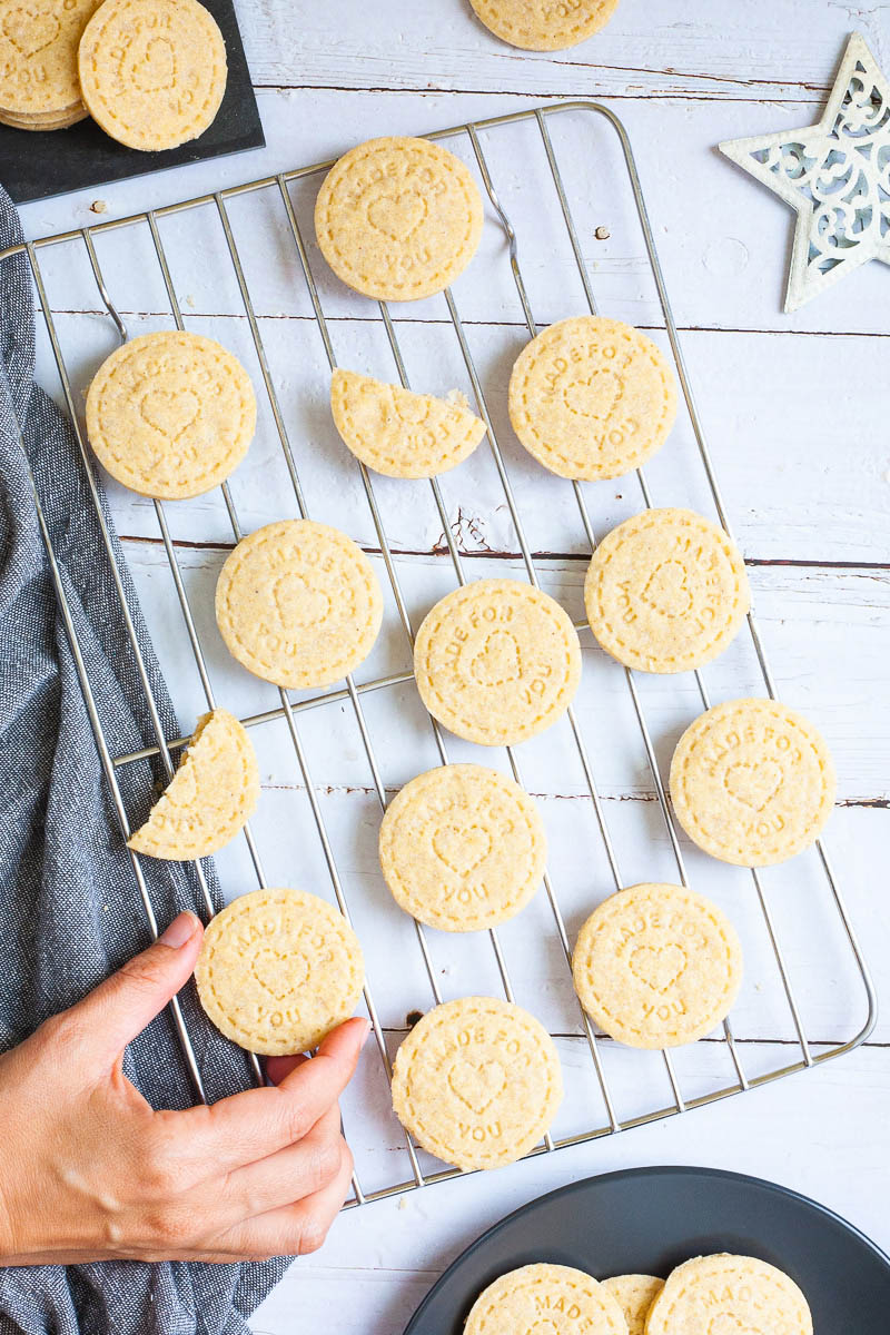 Several thin round cookies on wire rack. A hand is taking one cookie.