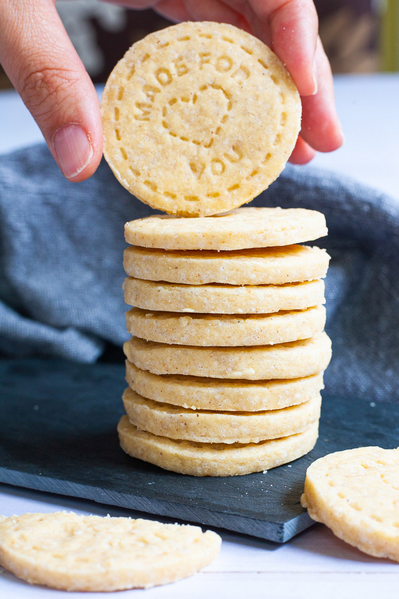 A stack of thin round cookies on a black board. A hand is holding the top cookie