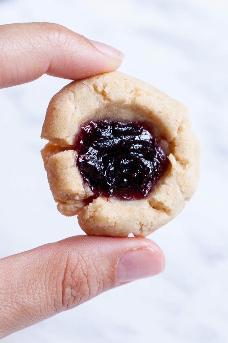 A hand is holding a round cookie filled with purple jam up close.