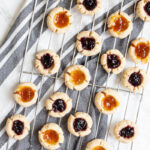 Several round cookies with orange and purple jam filling placed on a wire rack from above.