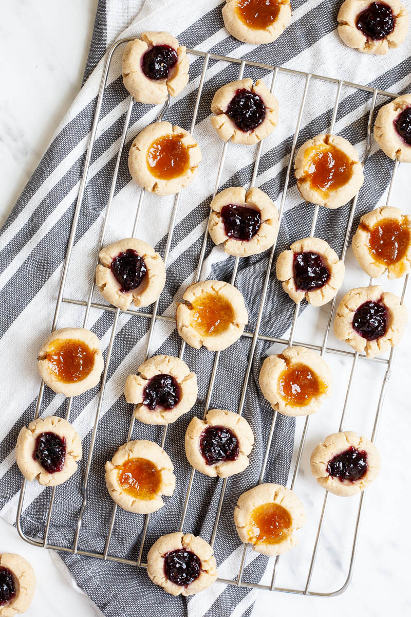 Several round cookies with orange and purple jam filling placed on a wire rack from above.