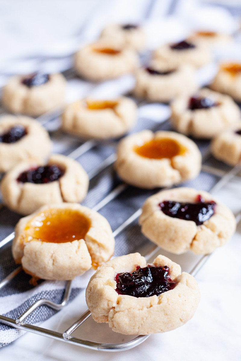 Several round cookies with orange and purple jam filling placed on a wire rack.