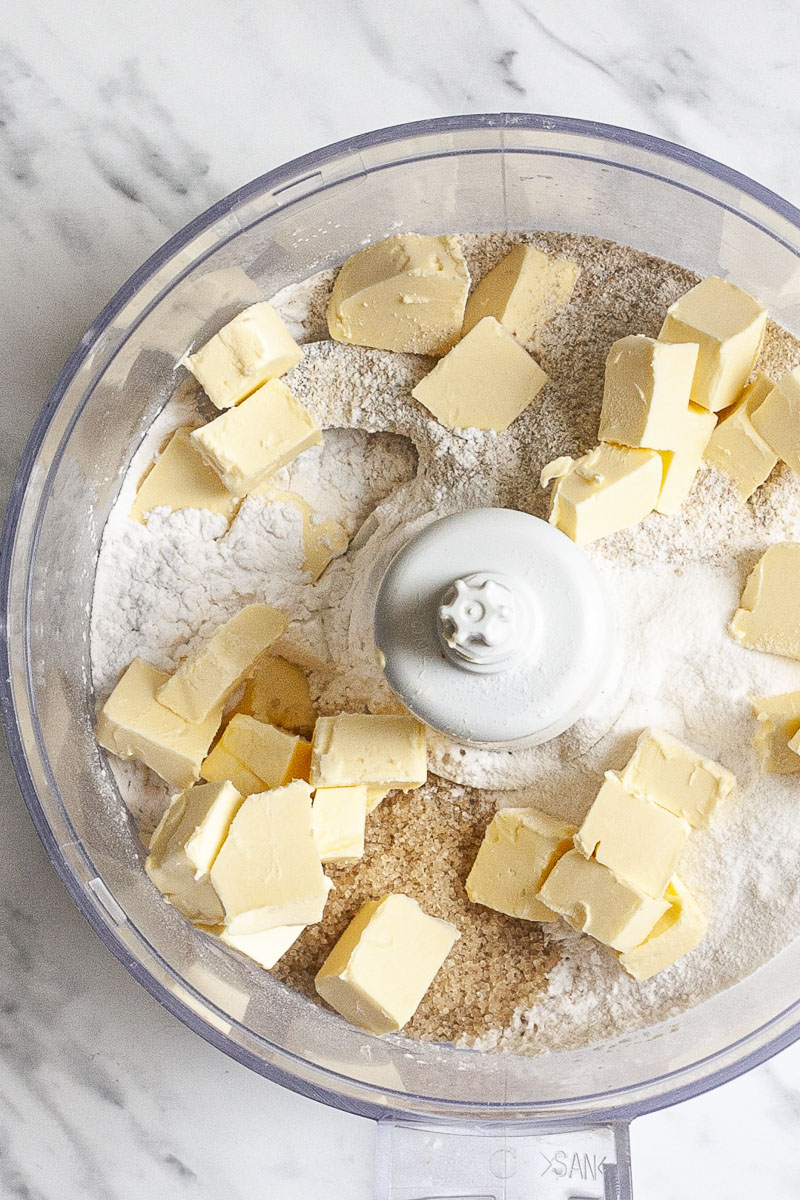 Food processor with flour, brown sugar and butter cubes.