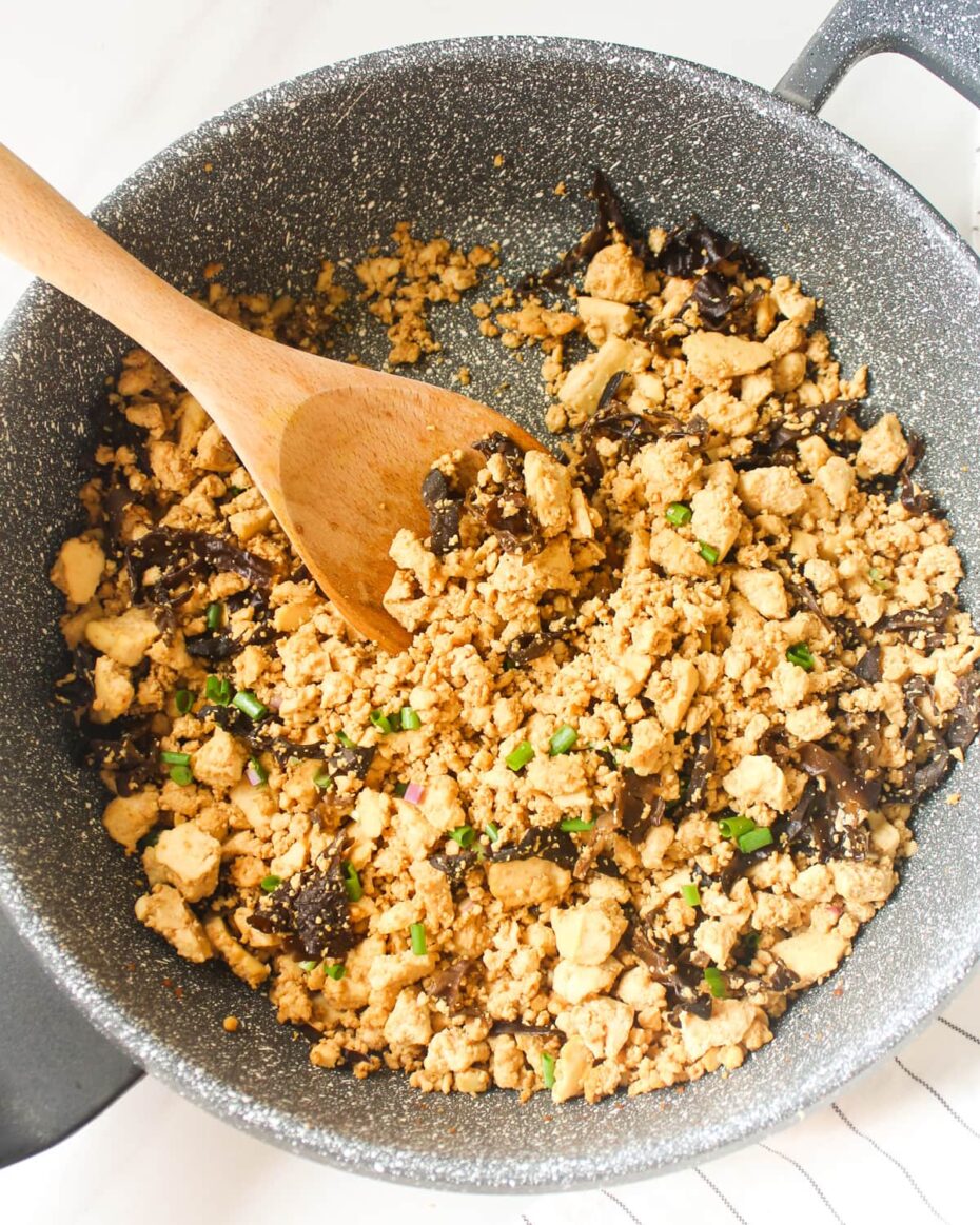 Grey frying pan from above with yellow crumbles and black wood ear mushroom pieces