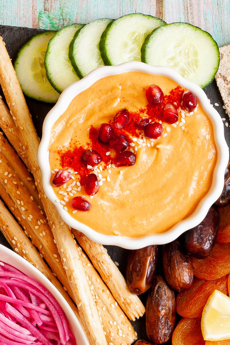 Black board with plenty of bowls, fruits and vegetables like cucumber, dried apricot, pomegranate seeds, dates, orange hummus