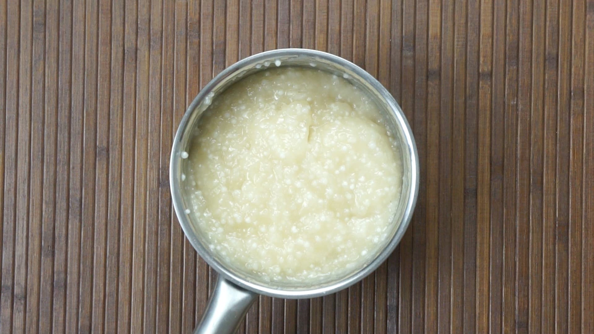 A saucepan on an induction hot plate with a thick light brownish - whitish liquid (milk) and small pearls.