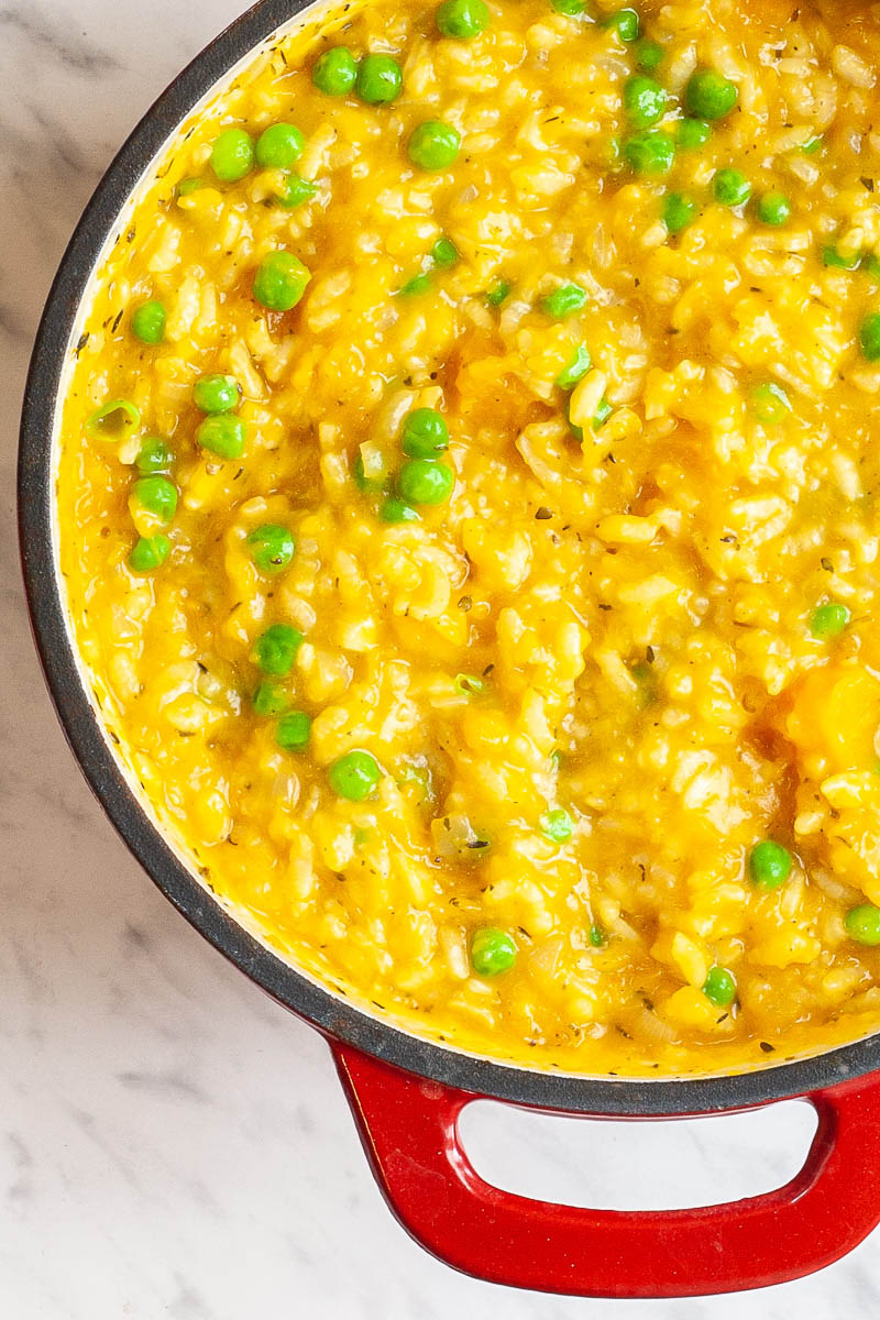 A red-white Dutch oven from above. with orange orange and veggie puree. Green peas are also visible.