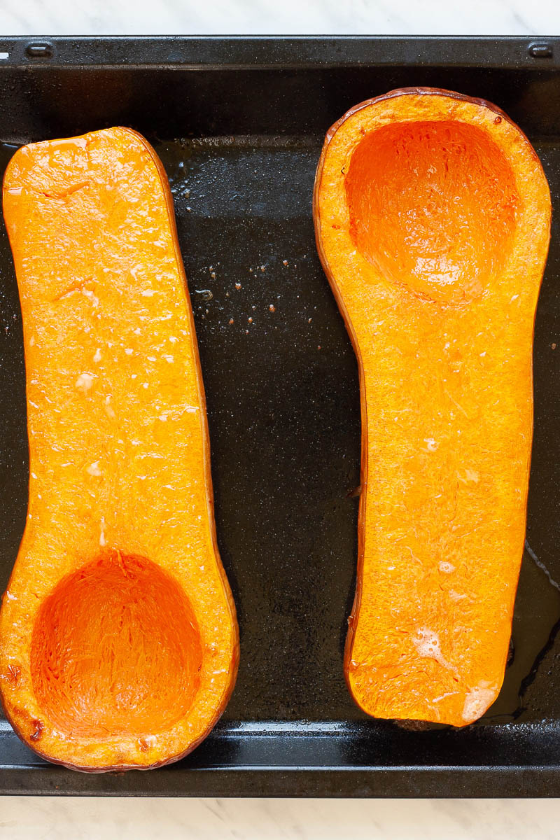 Black baking tray with 2 orange butternut squash cut in half after baking