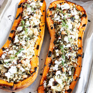 Silver baking tray with orange butternut squash cut in half and stuffed with rice, spinach, chickpeas, olives and crumbles feta cheese drizzled with black balsamic vinegar