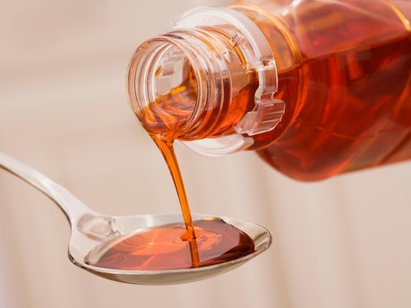 Redish brown syrup is poured into a spoon.