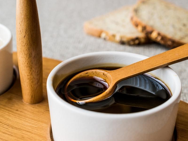 Black syrup in a small white bowl with a wooden spoon