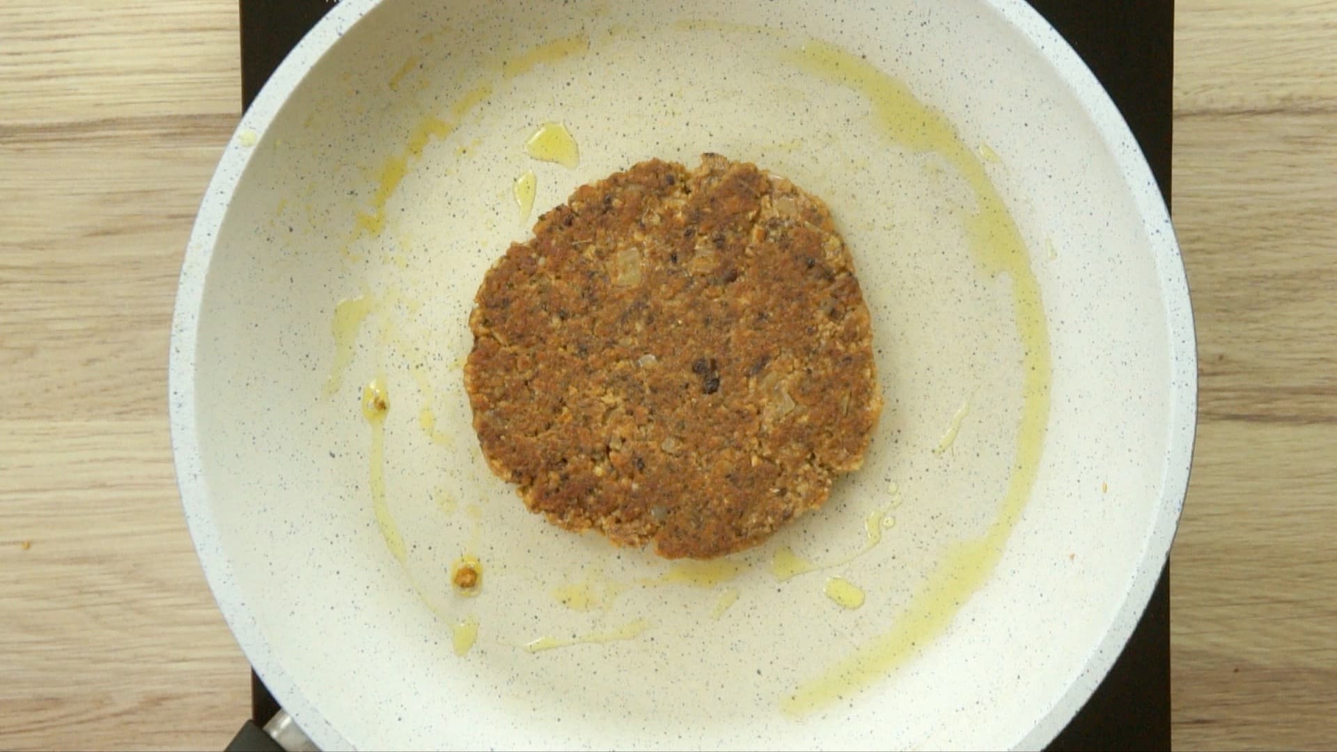 A white frying pan with one brown burger patty