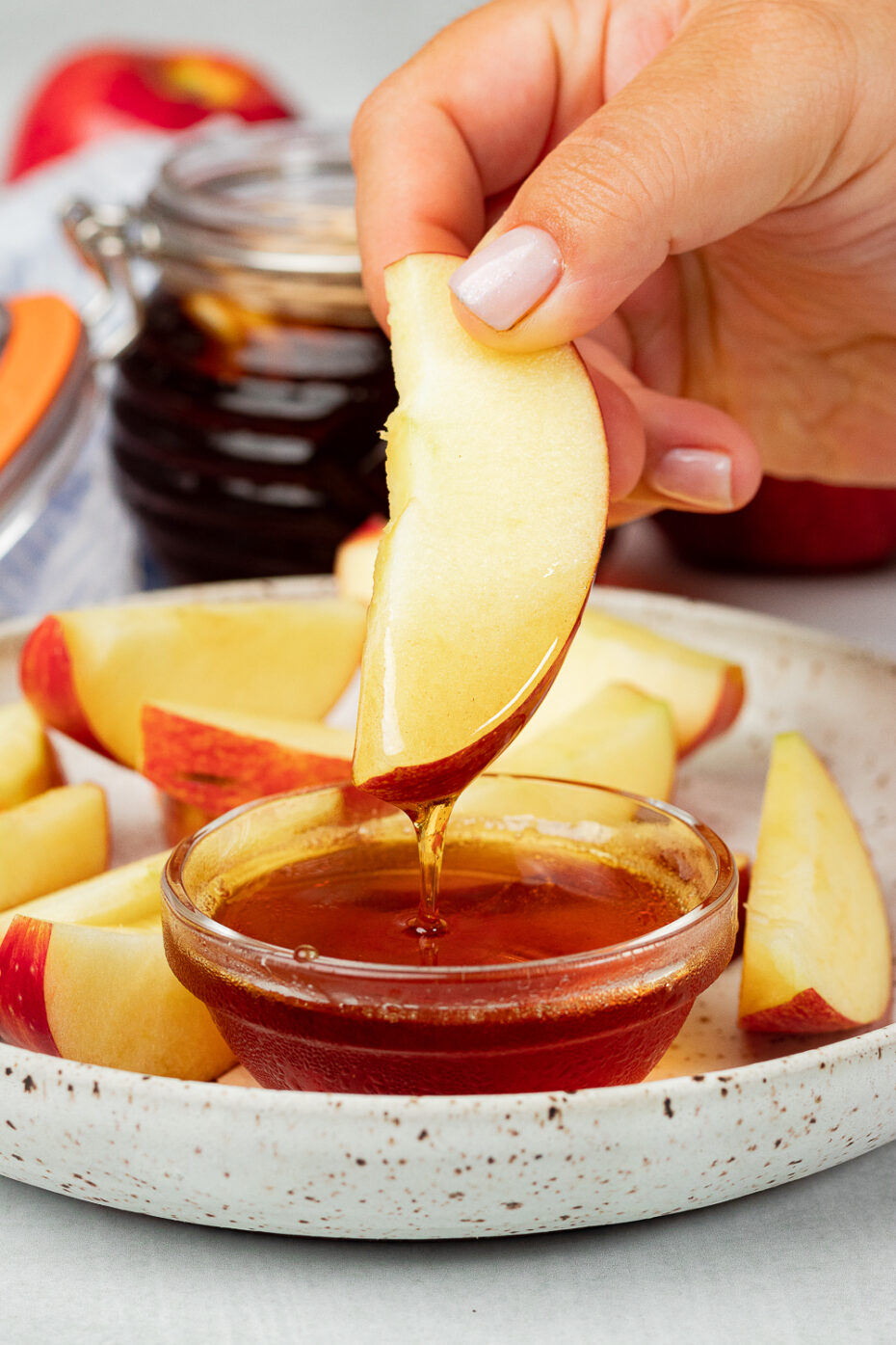 An apple slice is dipped in a dark brown syrup.