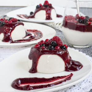 3 white plates with white panna cotta topped with a thick purple sauce and different berries.