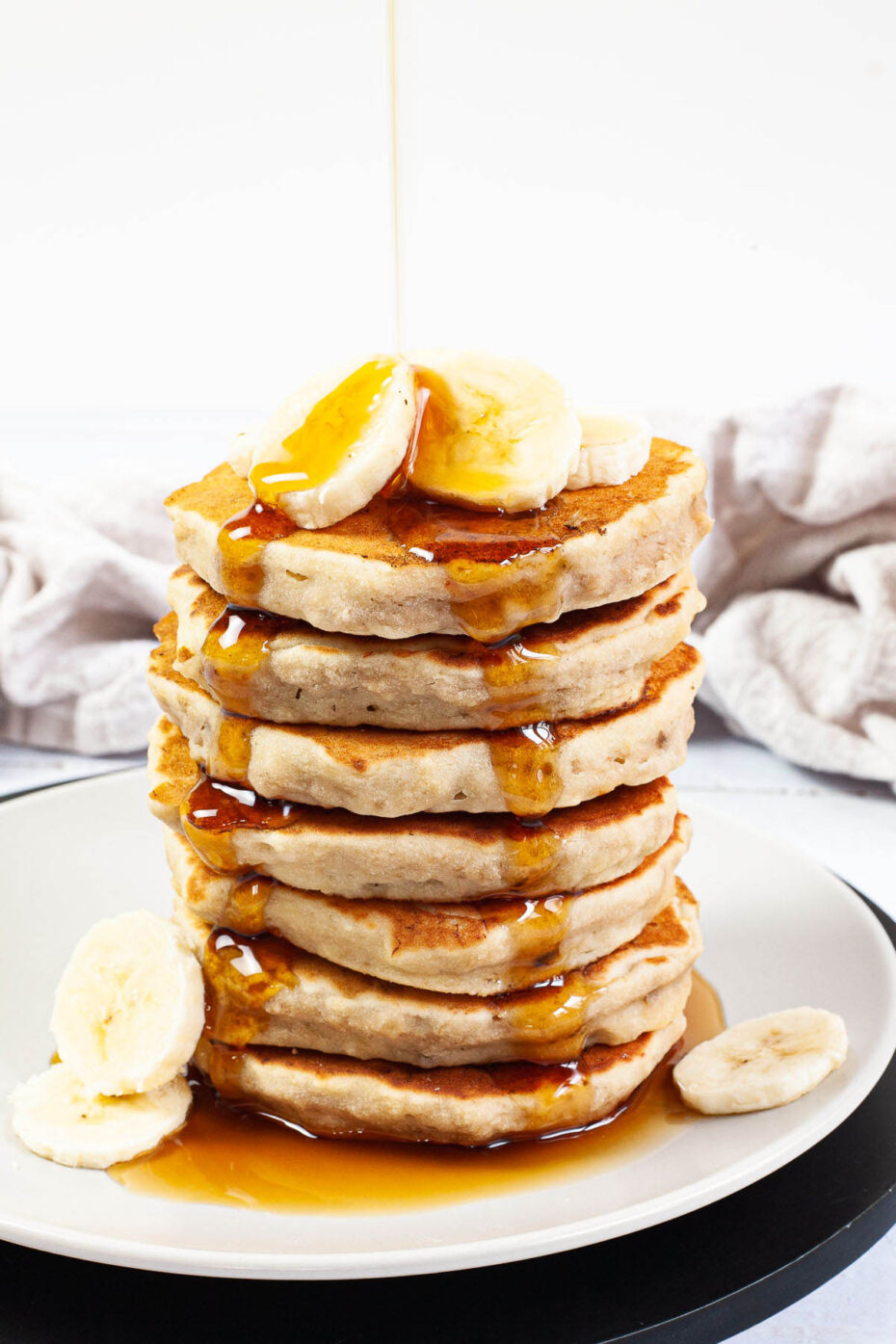 White plate with a stack of pancakes topped with banana slices