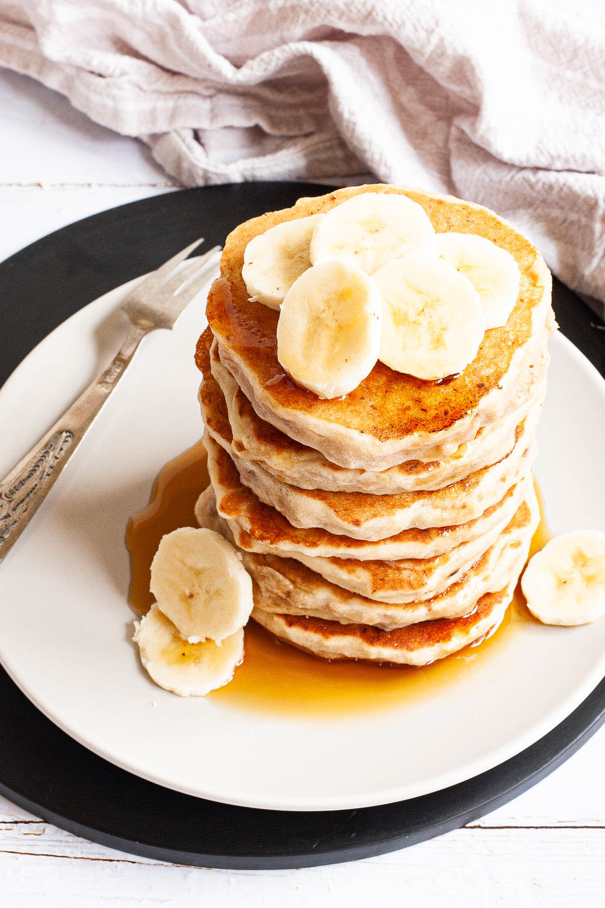 White plate with a stack of pancakes topped with banana slices
