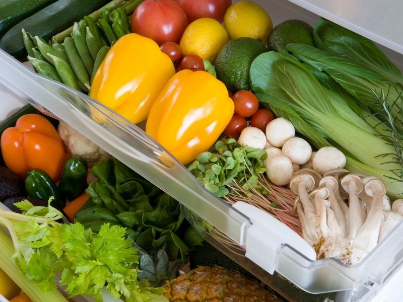 Different mushrooms and vegetables in the bottom drawer of a fridge