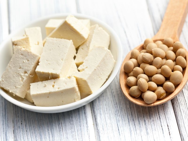 Tofu cubes in a white plate and a wooden spoon with dry soy beans