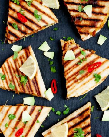 Several quesadilla triangles filled with black beans, red pepper, avocado slices sprinkled with fresh cilantro in a black board
