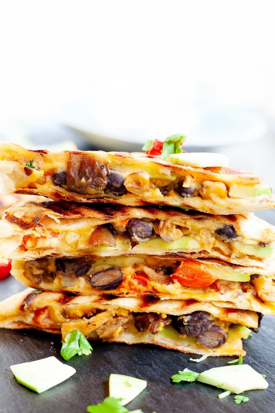 Stack of quesadilla triangles filled with black beans, red pepper, avocado slices sprinkled with fresh cilantro