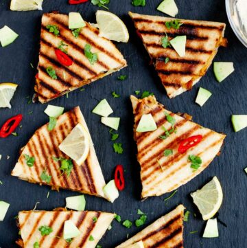 Several quesadilla triangles filled with black beans, red pepper, avocado slices sprinkled with fresh cilantro in a black board