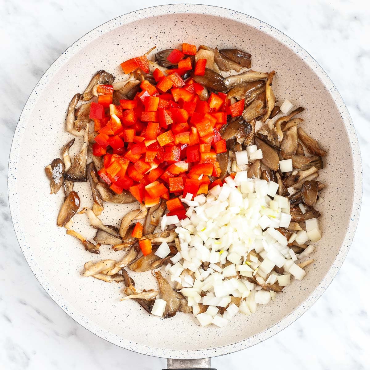 Brown mushroom shreds, chopped onion and chopped red pepper in a white frying pan