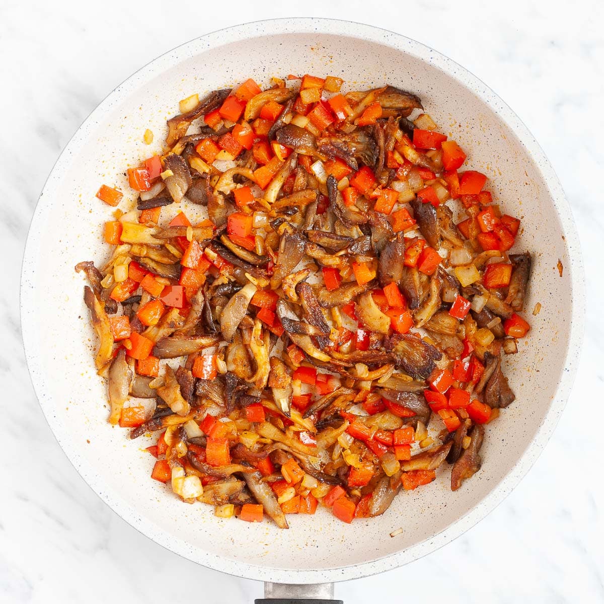 Crispy pan-fried chopped red pepper, onion, and mushroom shreds in a white frying pan