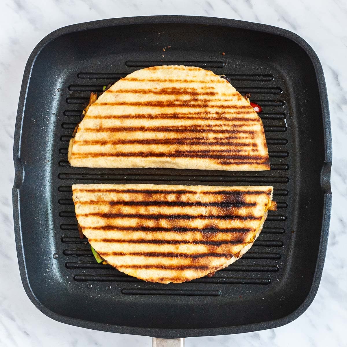 Two folded tortilla is frying on a grill pan.
