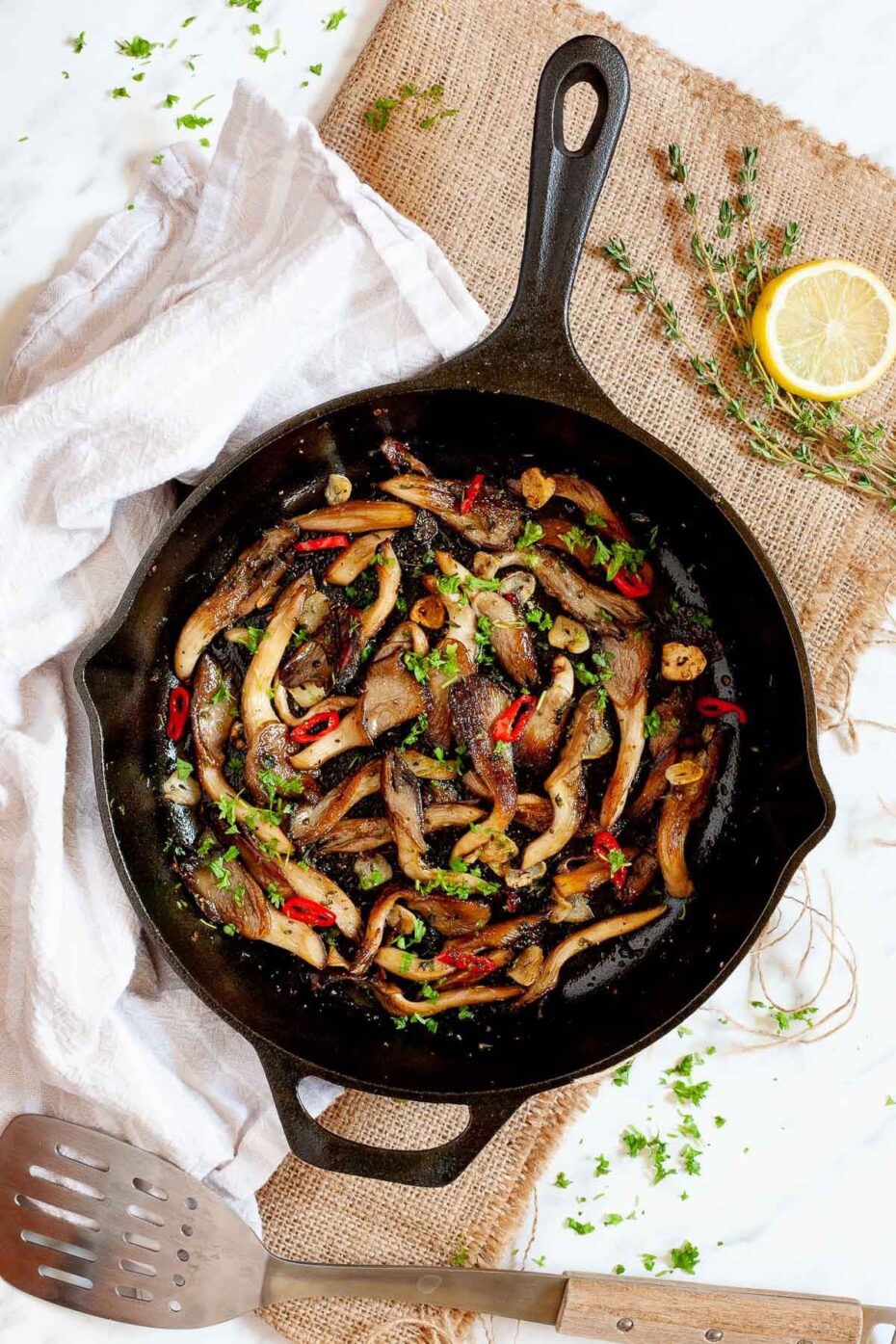 Black cast iron skillet from above with crispy brown oyster mushroom, sliced red pepper, garlic slices and chopped fresh green herbs.