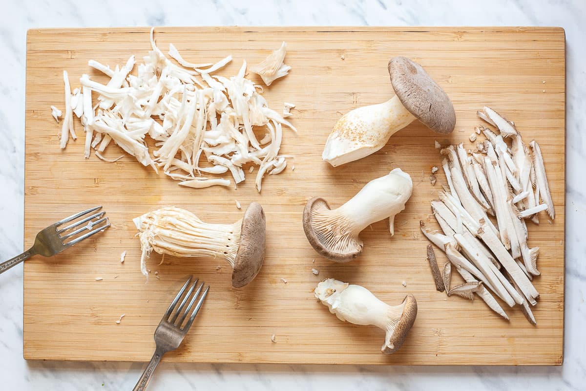 Wooden board and two forks with king oyster mushrooms in whole and in shreds