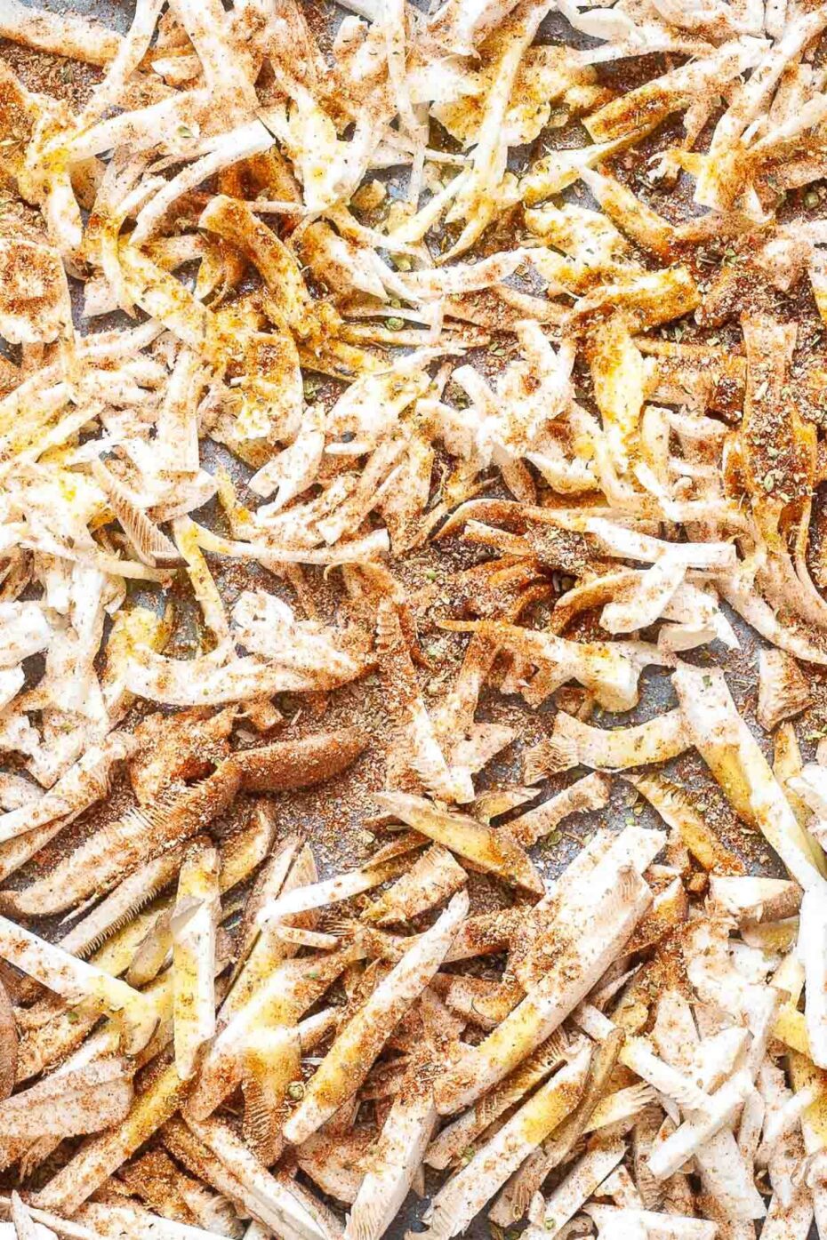 A parchment paper with shredded king oyster mushroom sprinkled with yellow and red spices