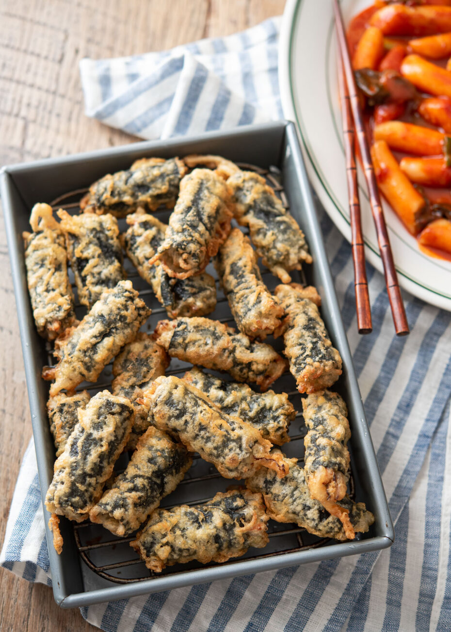 Dark green seaweed wrapped rolls fried in tempura is piled on a silver baking tray
