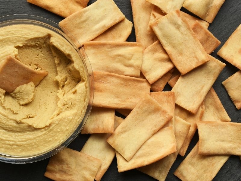 Small glass bowl with hummus and crispy rectangular crackers are all around it