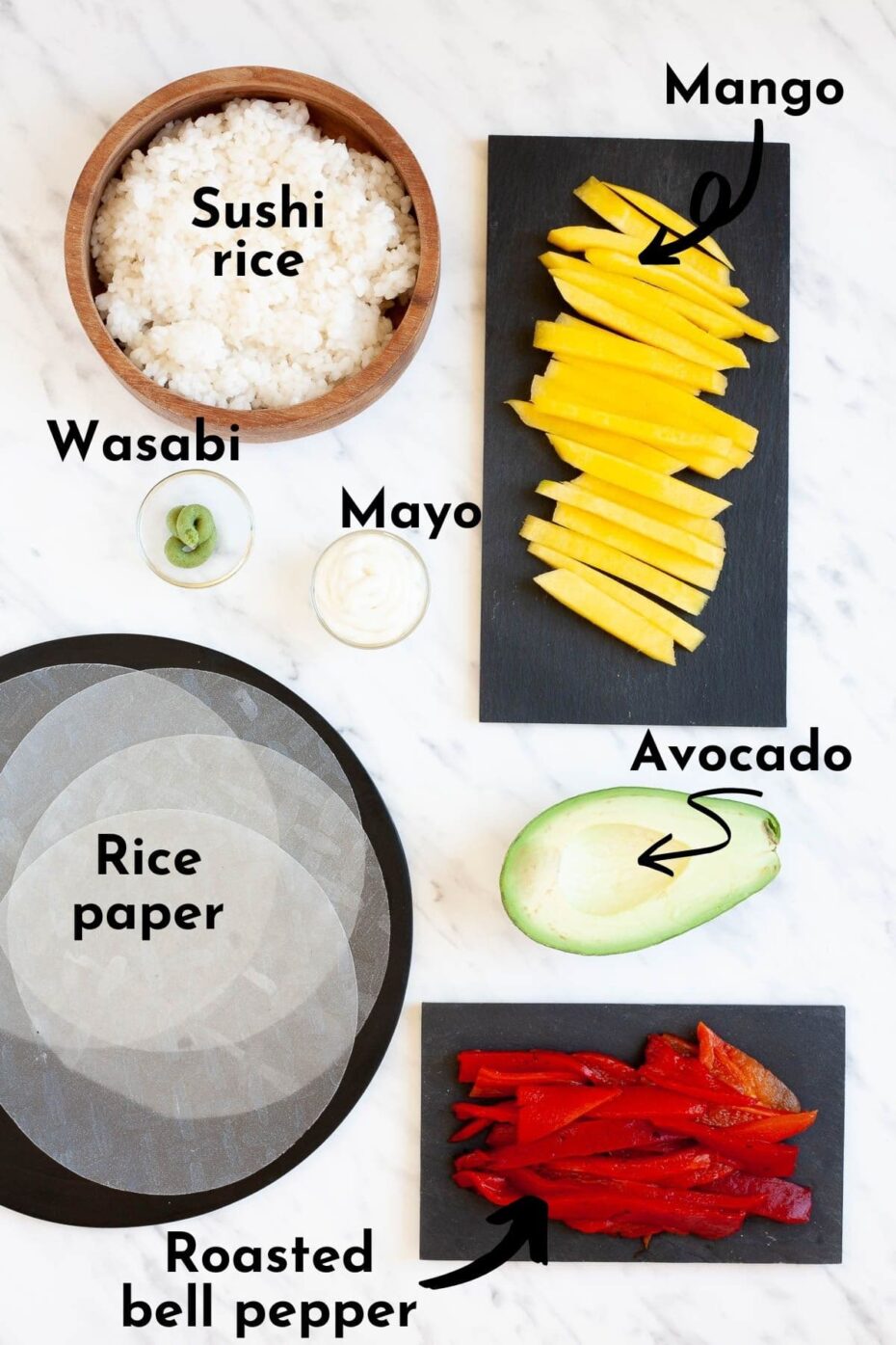 Ingredients to make rice paper sushi without seaweed is displayed in small bowls like rice, wasabi, mayo, mango slices, red pepper slices, half avocado and rice paper sheets