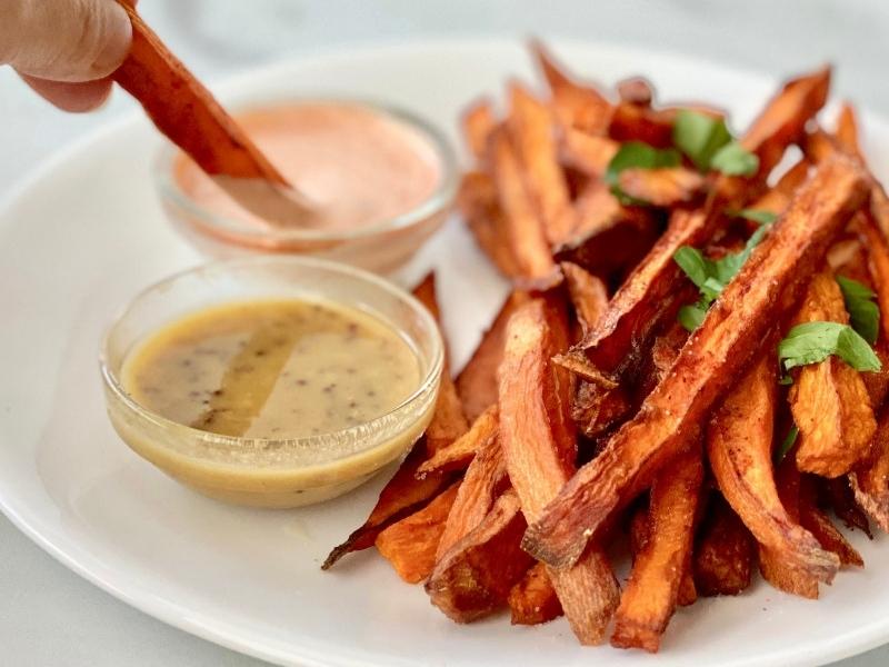 White plate with crispy sweet potato fries and two small glass of dipping sauce
