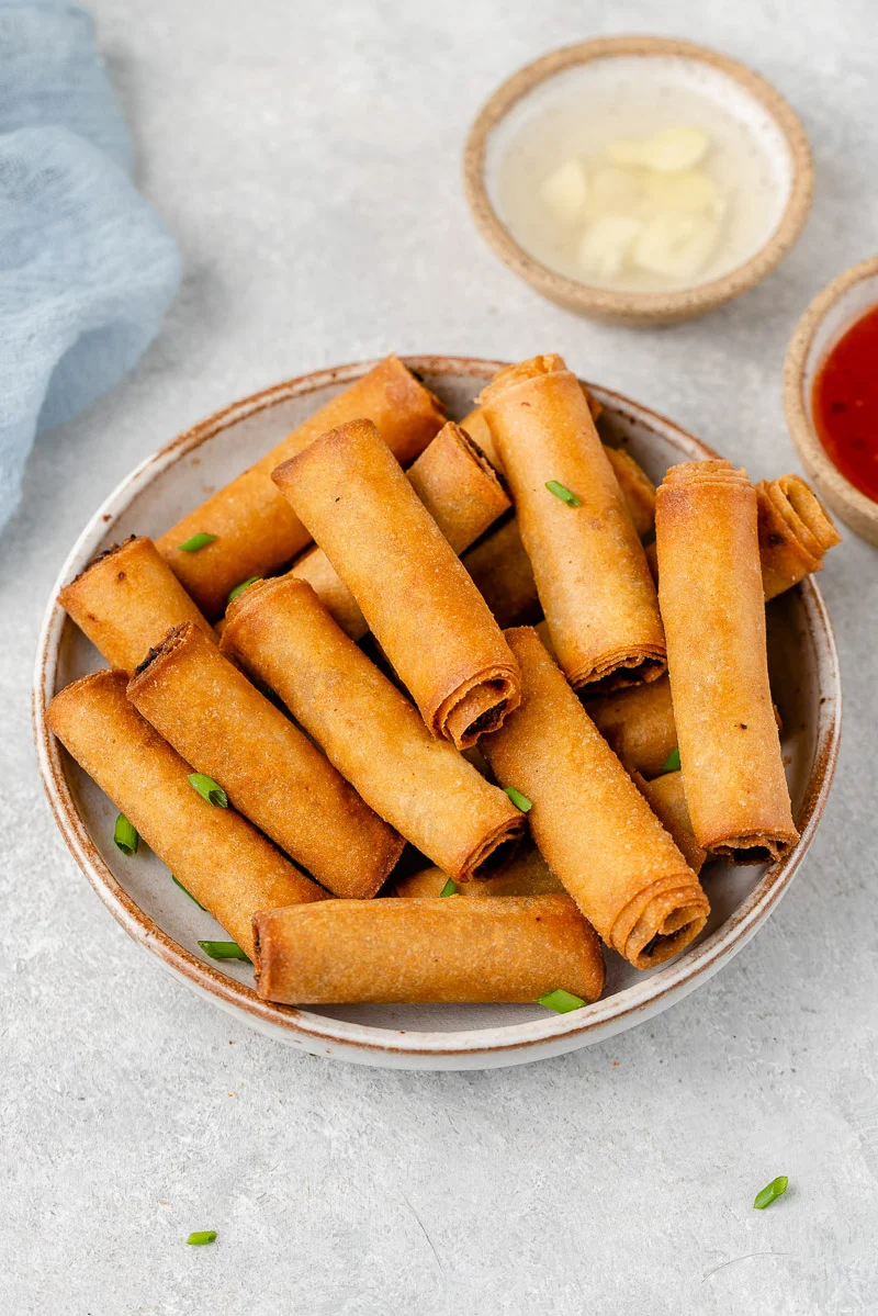 Brown crispy rolls are piled in a white bowl. The filling is not visible. 