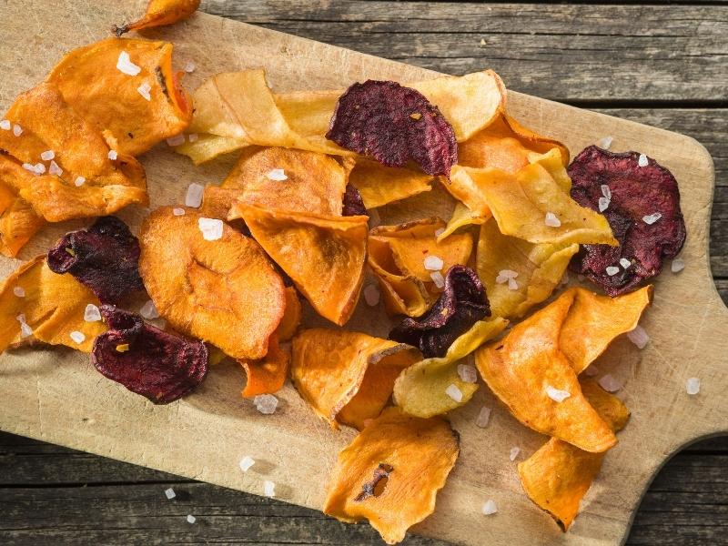 Orange and dark purple veggie chips on a wooden board