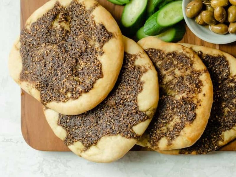 4 round flatbreads with dark brown herb sauce on a wooden board