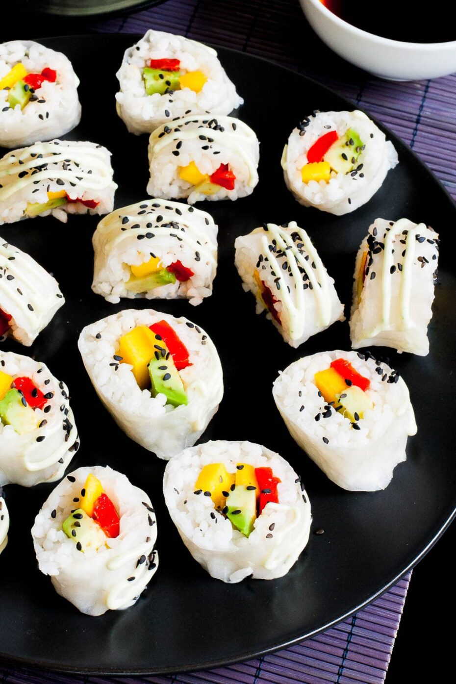 Large black round plate with a lot of white sushi rolls with colorful filling sprinkled with tiny black sesame seeds. 