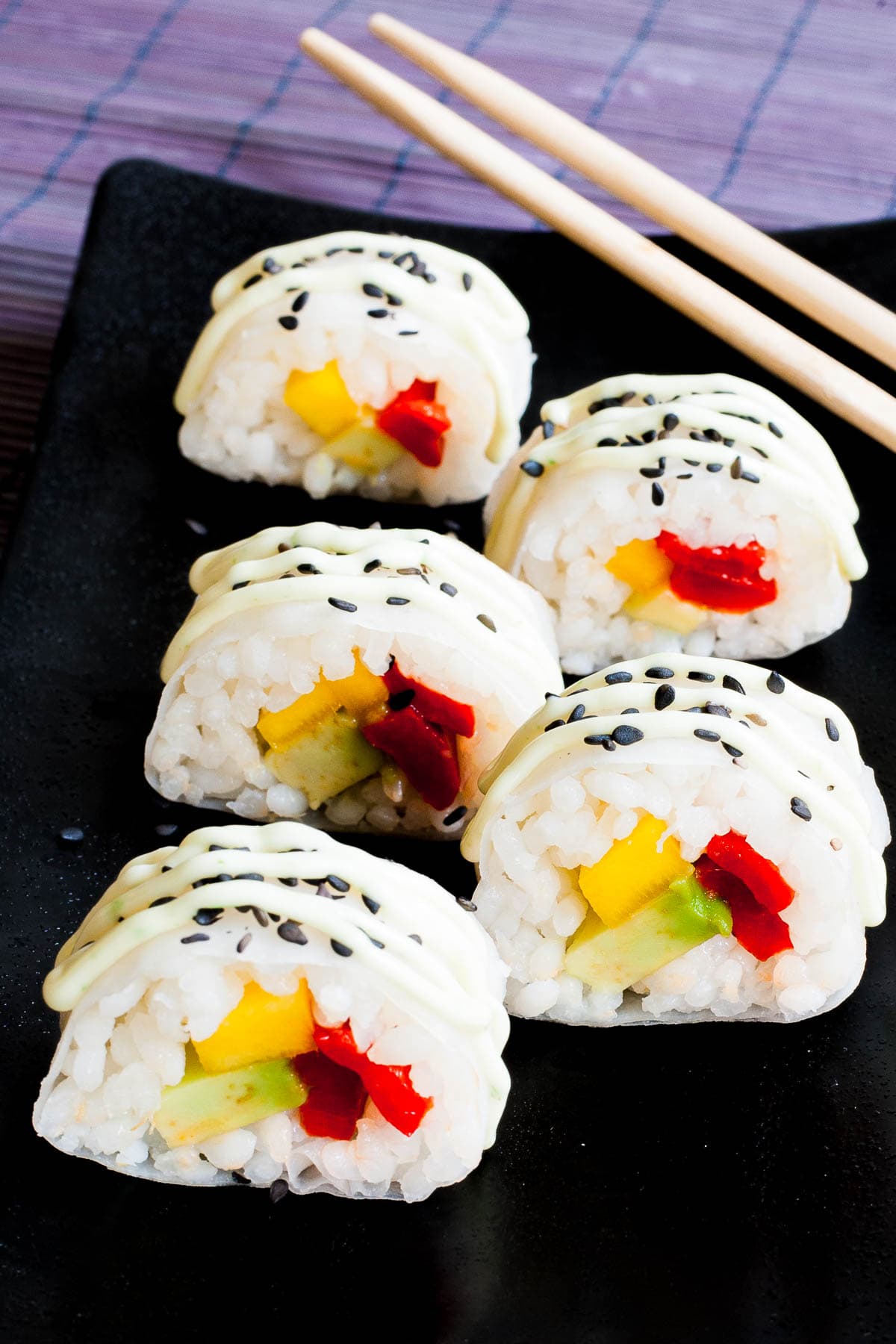 Black rectangle plate with 5 white sushi rolls with colorful filling sprinkled with tiny black sesame seeds